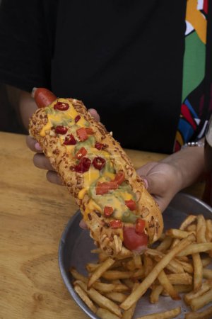Photo for Gourmet fast food. Closeup view of a woman eating a Mexican hot dog with guacamole, cheddar cheese and jalapenos, with french fries and a glass of beer. - Royalty Free Image