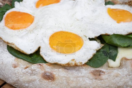 Photo for Food background. Closeup view of a pizza with mozzarella cheese, spinach and fried eggs, on the wooden table. - Royalty Free Image