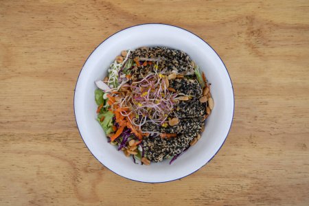 Photo for Healthy food. Top view of a salad with carrot, lettuce, peanuts, chicken breast breaded with seeds, soy sprouts and cabbage, in a white bowl on the wooden table. - Royalty Free Image