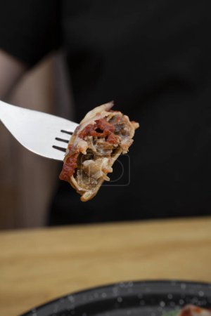 Téléchargez les photos : Pâtes farcies. Vue rapprochée d'une main tenant une fourchette, mangeant des sorrentinos farcies de tomates cerises et de veau, avec une sauce méditerranéenne et du provolone. - en image libre de droit