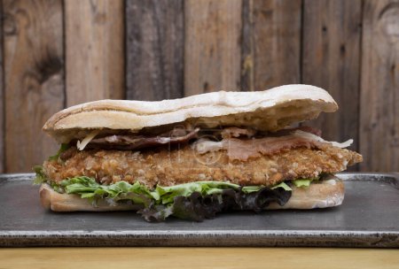 Photo for Gourmet sandwich. Closeup view of a multilayer sandwich with chicken fried steak, bacon, cheese and lettuce, with fried potatoes. - Royalty Free Image