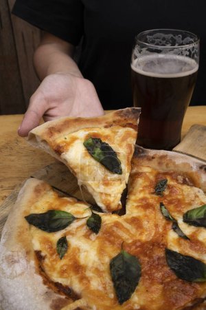 Téléchargez les photos : Pizza traditionnelle Margherita. Vue rapprochée d'une main féminine servant une tranche de pizza avec mozzarella et parmesan, sauce tomate et basilic, au restaurant. - en image libre de droit