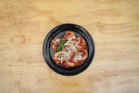 Foto de Pastas rellenas. Vista superior de los sorrentinos con salsa de tomate mediterráneo y queso provolone en un plato negro sobre la mesa de madera. - Imagen libre de derechos