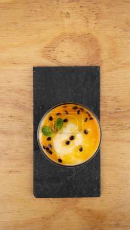 Photo for Fruity desserts. Closeup view of a glass with passion fruit mousse, in a black dish on the wooden table. - Royalty Free Image