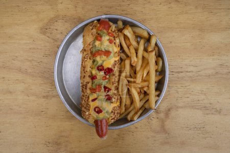 Téléchargez les photos : Restauration rapide gastronomique. Vue de dessus d'un hot dog avec guacamole, chilis, fromage cheddar et frites, dans un plat métallique avec un fond en bois. - en image libre de droit