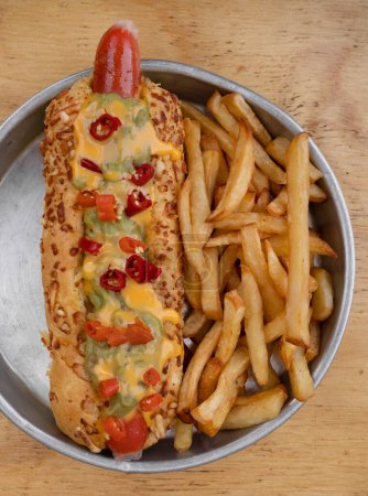 Foto de Hot dog con cebolla crujiente, pepino en rodajas y mostaza con miel, con papas fritas en un plato de metal. - Imagen libre de derechos
