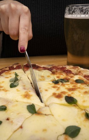 Foto de Mujer sosteniendo un cuchillo, cortando una pizza tradicional de mozzarella. - Imagen libre de derechos