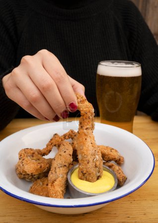 Photo for Eating at the restaurant. View of woman dipping a fried breaded chicken stick in curry mayonnaise. - Royalty Free Image