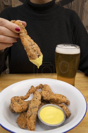Photo for Eating at the restaurant. View of woman holding a fried breaded chicken stick dipped in curry mayonnaise. - Royalty Free Image