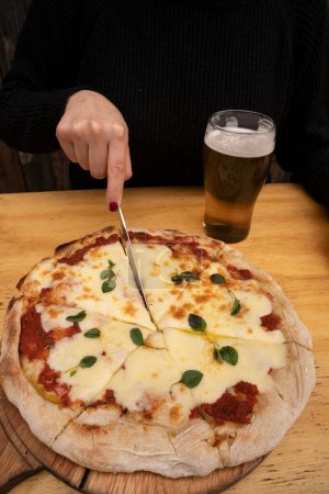 Téléchargez les photos : Femme tenant un couteau, tranchant une pizza mozzarella traditionnelle. - en image libre de droit