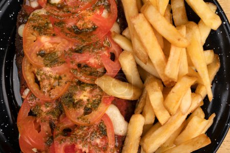Photo for Milanesa napolitana. Top view of fried breaded steak with mozzarella cheese, tomato, garlic, basil and french fries. - Royalty Free Image
