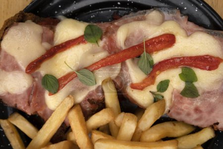 Téléchargez les photos : Vue du dessus du plat milanesa, steak de pain frit, avec fromage mozzarella, jambon, origan, poivron rouge grillé et pommes de terre frites. - en image libre de droit