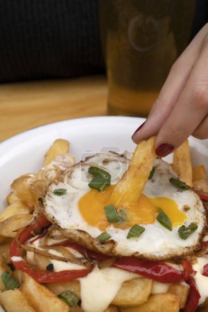 Téléchargez les photos : Manger des frites gastronomiques. Femme trempant une pomme de terre frite dans le jaune d'un œuf grillé. - en image libre de droit