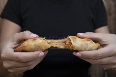 Photo for Finger food. Closeup view of a woman cutting a traditional empanada, and stretching the provolone cheese. - Royalty Free Image