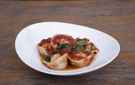 Pasta. Vista de cerca de una agnolottis con salsa de tomate y pesto, en un plato blanco en la mesa de madera del restaurante.