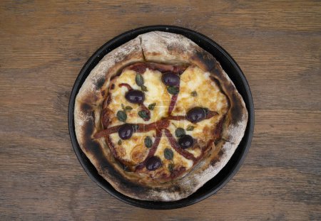 Téléchargez les photos : Une pizza. Vue de dessus d'une pizza au fromage mozzarella, poivrons rouges grillés, jambon, olives noires et feuilles d'origan frais, dans une poêle à pizza sur la table en bois. - en image libre de droit