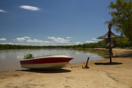 Vista panorámica de la orilla del río en un día soleado de verano. Un barco en la arena en primer plano y la selva tropical en el fondo reflejado en el agua.