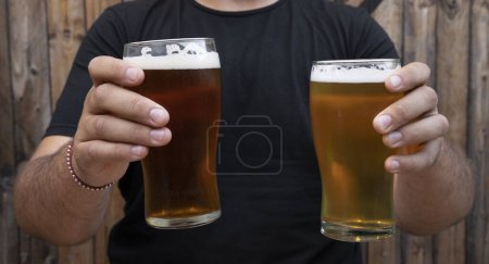 Téléchargez les photos : Bonne heure. Vue rapprochée d'un homme tenant deux verres de bière avec un fond en bois. - en image libre de droit