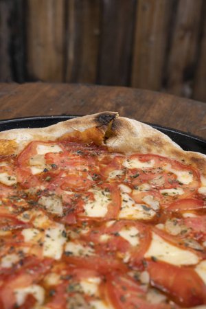 Téléchargez les photos : Vue rapprochée d'une pizza napolitaine traditionnelle avec fromage mozzarella, ail rôti, tomates tranchées et feuilles d'origan fraîches. - en image libre de droit