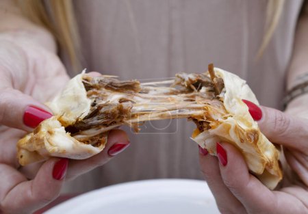 Photo for Eating empanadas. Closeup view of a woman hands breaking a flank steak meat and provolone cheese empanada. - Royalty Free Image