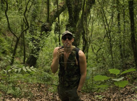 Foto de Guerrilla. Retrato de un adulto caucásico joven con paños camuflados en la selva. Musculoso hombre senderismo con gafas de sol y fumar. - Imagen libre de derechos