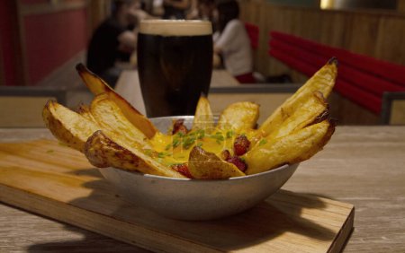 Foto de Comida Americana. Patatas asadas con queso cheddar y una cerveza negra en el bar. - Imagen libre de derechos