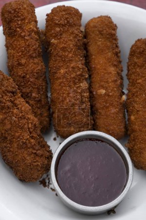 Photo for Top view of fried breaded mozzarella sticks with dipping barbecue sauce in a white bowl on the red wooden table. - Royalty Free Image