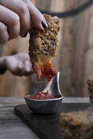 Photo for Finger food. Closeup view of a caucasian woman's hand dipping a fried mozzarella stick in ketchup sauce, in the restaurant. - Royalty Free Image