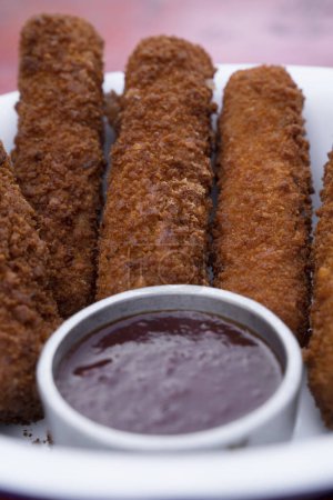 Photo for Top view of fried breaded mozzarella sticks with dipping barbecue sauce in a white bowl on the red wooden table. - Royalty Free Image