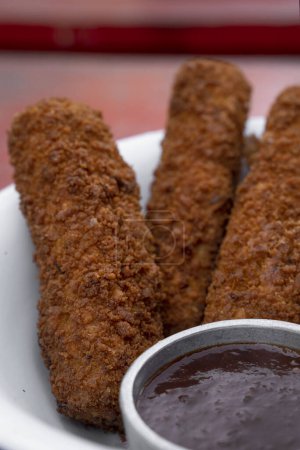 Photo for Closeup view of fried breaded mozzarella sticks with dipping barbecue sauce in a white bowl on the red wooden table. - Royalty Free Image