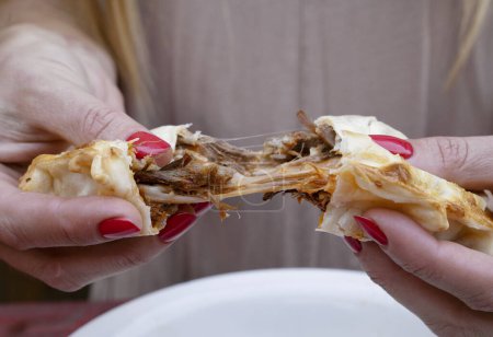Photo for Eating empanadas. Closeup view of a woman hands breaking a flank steak meat and provolone cheese empanada. - Royalty Free Image