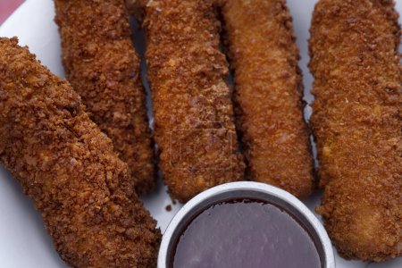 Photo for Finger food. Top view of fried breaded mozzarella sticks with dipping barbecue sauce in a white bowl on the red wooden table. - Royalty Free Image
