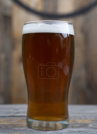 Téléchargez les photos : Brew. Vue rapprochée d'une ale ambre avec une mousse parfaite dans un verre sur la table en bois. - en image libre de droit