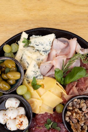 Salchichas. Vista superior de un plato con salami en rodajas, queso, queso azul, boconccinos italianos, nueces, jamón, jamón curado y aceitunas verdes, sobre la mesa de madera.