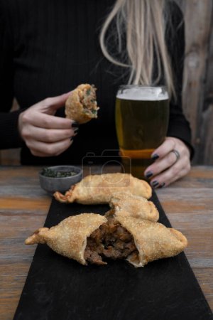 Photo for Eating empanadas at the restaurant. Closeup view of a caucasian woman having fried meat empanadas with traditional chimichurri sauce. - Royalty Free Image