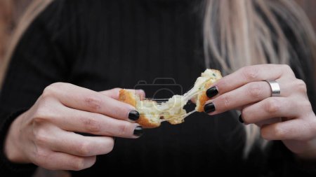 Food. Closeup view of a woman stretching the cheese of a sliced potato and mozzarella croquette.
