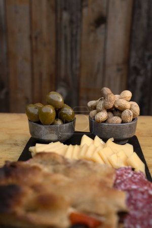 Antipasto. Enfoque selectivo en aceitunas verdes y cacahuetes, en un plato de embutidos con queso, salami y pan de focaccia. 