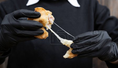 Photo for Finger food. Closeup view of a female chef wearing gloves, stretching a traditional cheese and ham empanada. - Royalty Free Image