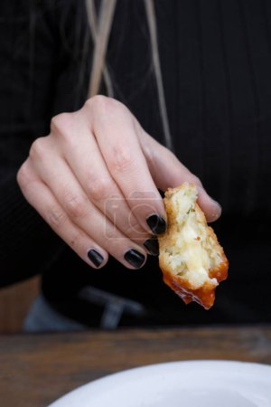 Eating cheese balls at the restaurant. Closeup view of a caucasian woman's hand, holding a potato and mozzarella croquette dipped in sweet chili sauce.