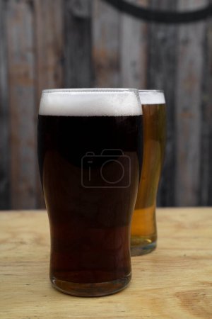 Two glasses of beer, a honey golden one and a black stout beer, with a rustic wooden background