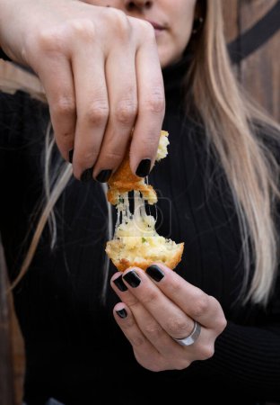 Finger food. Nahaufnahme einer Frau, die den Käse einer in Scheiben geschnittenen Kartoffel und Mozzarella-Krokette dehnt. 