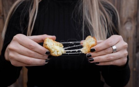 Comida para dedos. Vista de cerca de una mujer estirando el queso de una croqueta de patata y mozzarella en rodajas. 