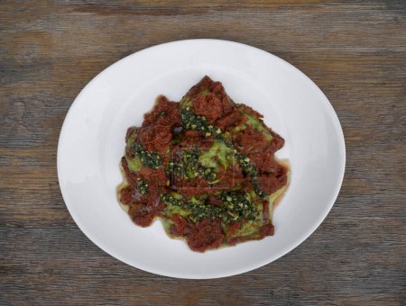 Pasta. Top view of spinach ravioli with tomato sauce and pesto, in a white dish on the wooden table. 