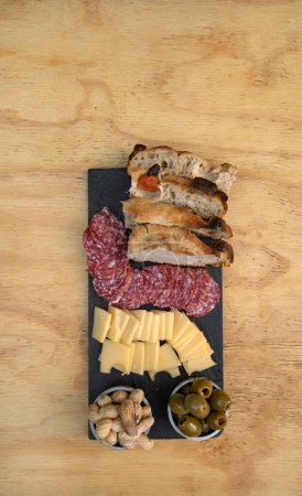 Antipasto. Vista superior de un plato con salami en rodajas, queso, cacahuetes focaccia y aceitunas verdes en la mesa de madera.
