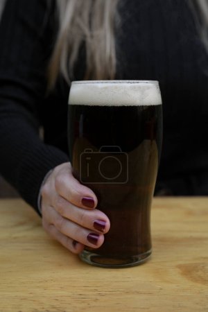 Drinks. Closeup view of a young caucasian female hand holding a glass of black beer in the bar.