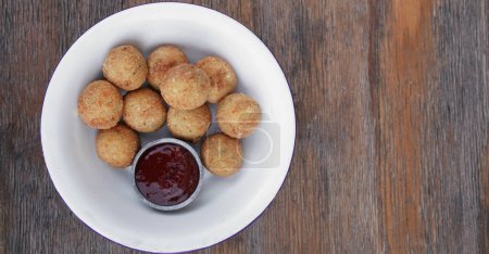 Cheese balls. Top view of potato and mozzarella cheese croquettes with sweet chili dipping sauce, in a white bowl on the wooden table.