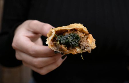 Photo for Finger food. Traditional meat empanadas. Closeup view of a woman hand holding a meat empanada with traditional chimichurri sauce. - Royalty Free Image