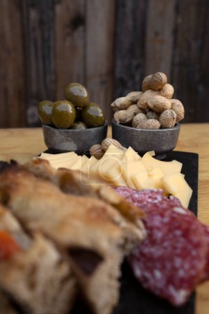 Antipasto. Closeup view of green olives and peanuts, in a cold cuts dish with cheese, salami and focaccia bread.