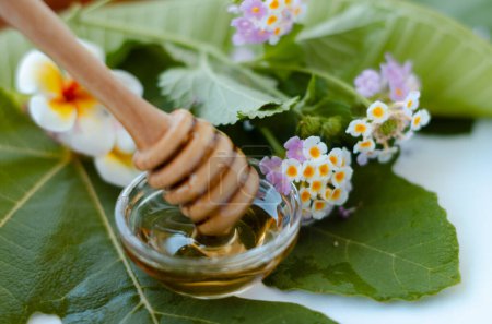 Photo for Honey spoon with honey and a frangipani and lantana flower - Royalty Free Image