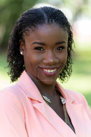 Closeup outdoor portrait of a beautiful young black woman with a sister loc hairstyle wearing a blazer dress smiling